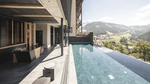 Friedrich ist DAS Boutiquehotel in den Dolomiten Infinity-Pool mit Bergblick an modernem Hotel in sonniger Landschaft