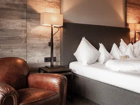 Friedrich ist DAS Boutiquehotel in den Dolomiten Gemütliches Hotelzimmer mit Ledersessel, Nachttischlampen und weißem Bett