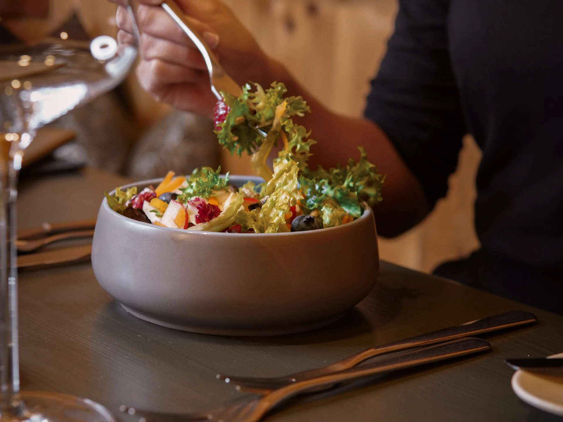 Friedrich ist DAS Boutiquehotel in den Dolomiten Person isst frischen gemischten Salat mit Gabel an einem Esstisch